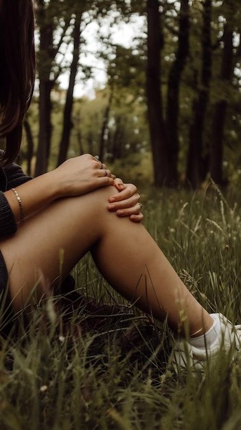 Low section of woman with knee pn sitting on field in forest