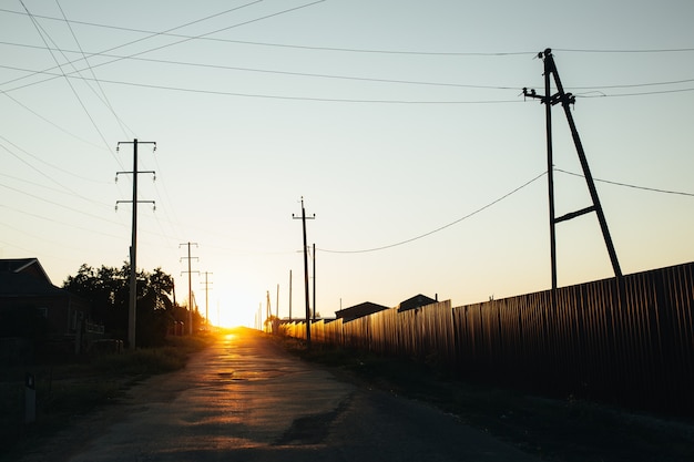 Low sunset sun shines on a rural road. There are private buildings to the left of the road.