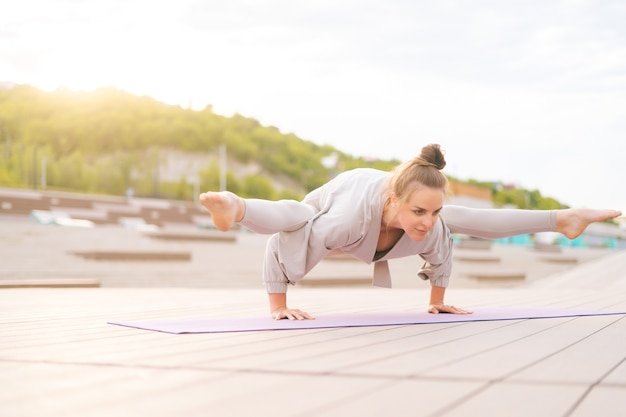 Lowangle view of flexible young yogini woman practicing yoga exercisers on fitness mat on summer day