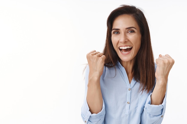 Lucky happy cheerful brunette mother triumphing son won, achieve goal, fist pump joyfully smiling, support daughter football match, grinning, celebrating good news, victory sign, white wall