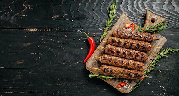 Lula kebab, traditional Caucasian dish. On the black background of the concrete, on a chopping board, with ketchup, spices and tomatoes copy space above