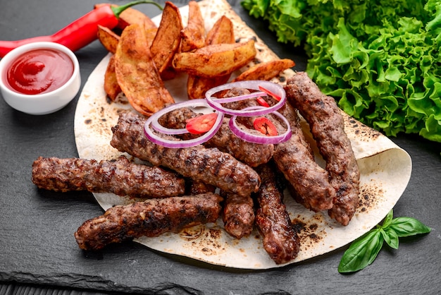 Lula kebab with potatoes, vegetables and sauce, on a black surface