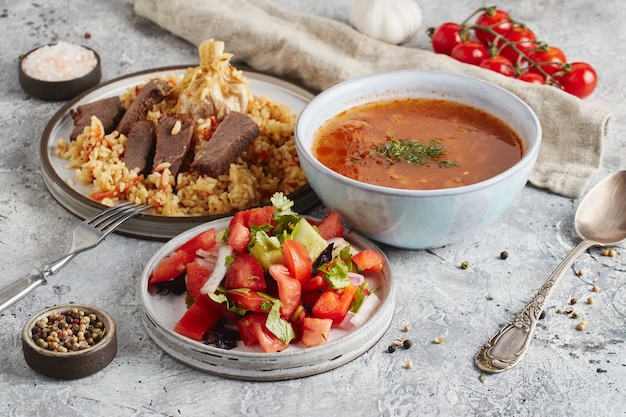 Lunch in bowl and plates with fork and spoon, kitchen cloth and tomatoes on light marble background