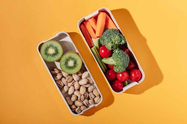 Lunch box with fresh vegetables fruits and nuts on yellow background