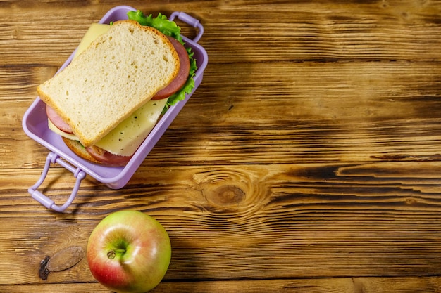 Lunch box with sandwiches and apple on a wooden table Top view copy space