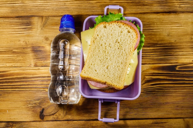 Lunch box with sandwiches and bottle of water on a wooden table Top view