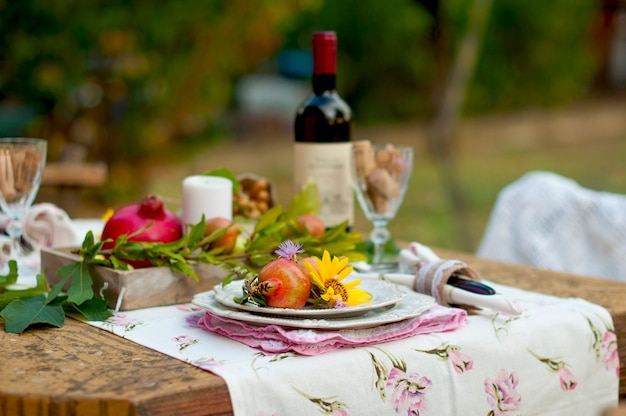 Lunch is romantic in autumn garden, atmosphere of holiday and coziness. Autumnal dinner in the open air with wine and fruit. Decor table with flowers and pomegranate. Vintage photo.