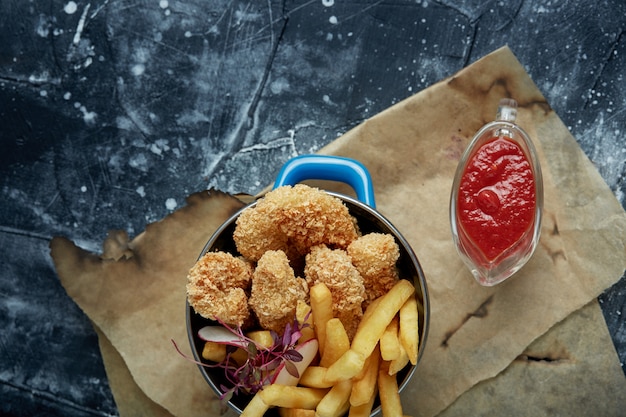 Lunch or snack - fried chicken strips and french fries in a metal pan with tomato sauce. Craft paper on the space.