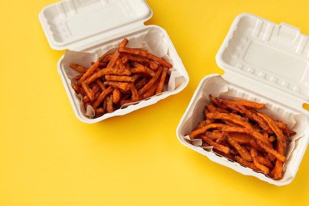 Lunchboxes with fries sweet potato drink and sauce on yellow table Flat lay top view food delivery concept