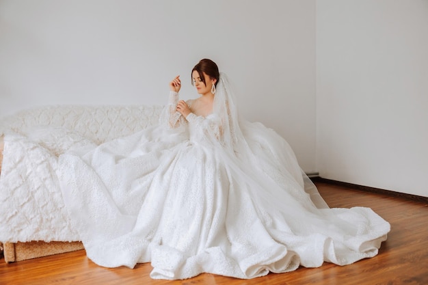 A luxurious bride with a beautiful hairstyle and a gorgeous dress is getting ready for the wedding ceremony in the morning Morning photo of the bride at home or in a hotel room Professional makeup