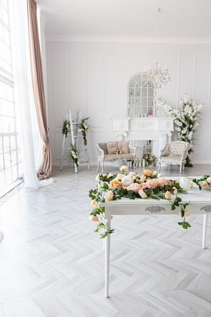 Luxurious bright spacious guest room with beautiful chic furniture a huge floor-to-ceiling window in a royal style is decorated with green plants, white walls with stucco and a fireplace