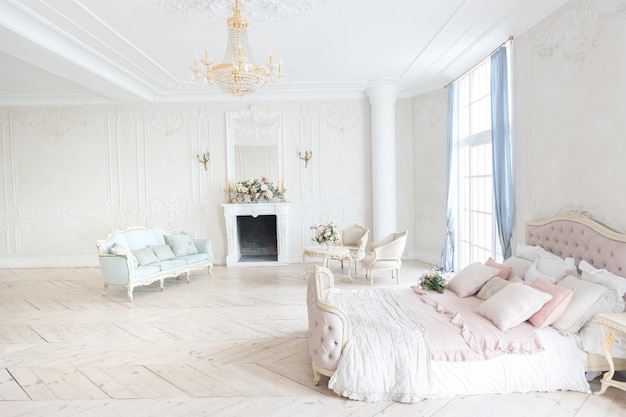 Luxurious light interior in the Baroque style. A spacious room with a road chic beautiful furniture, a fireplace and flowers. plant stucco on the walls and light wood parquet