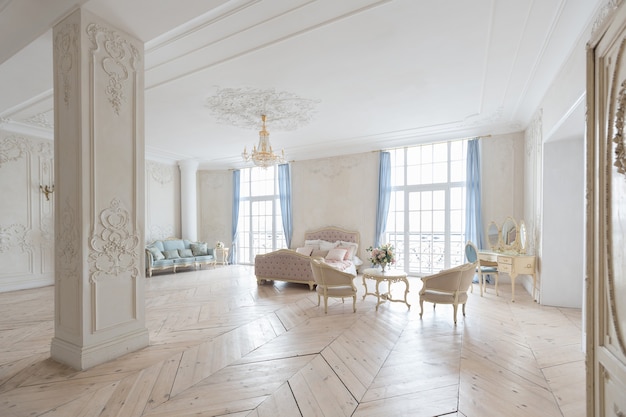 Luxurious light interior in the Baroque style. A spacious room with a road chic beautiful furniture, a fireplace and flowers. plant stucco on the walls and light wood parquet