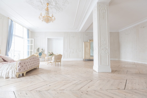 Luxurious light interior in the Baroque style. A spacious room with a road chic beautiful furniture, a fireplace and flowers. plant stucco on the walls and light wood parquet