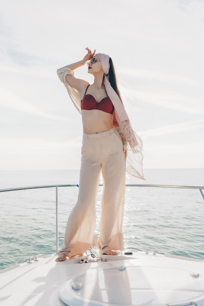 Luxurious stylish woman in summer clothes posing on a yacht in the sun going on vacation