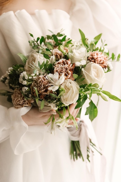 A luxurious wedding bouquet with roses and carnations in the hands of the bridexA