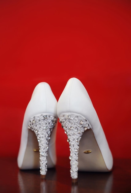 Photo luxurious white wedding shoes with high heels on a red background rear view