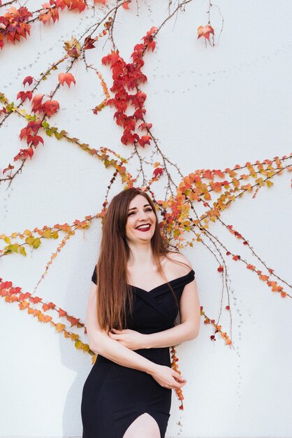 A luxurious young woman in a black dress laughs, poses against the wall, enjoys a rich life