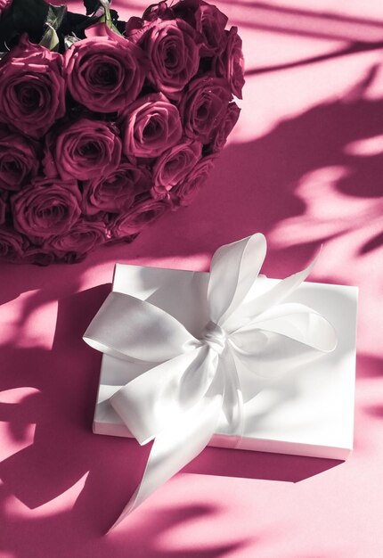 Luxury holiday silk gift box and bouquet of roses on pink background romantic surprise and flowers as birthday or Valentines Day present