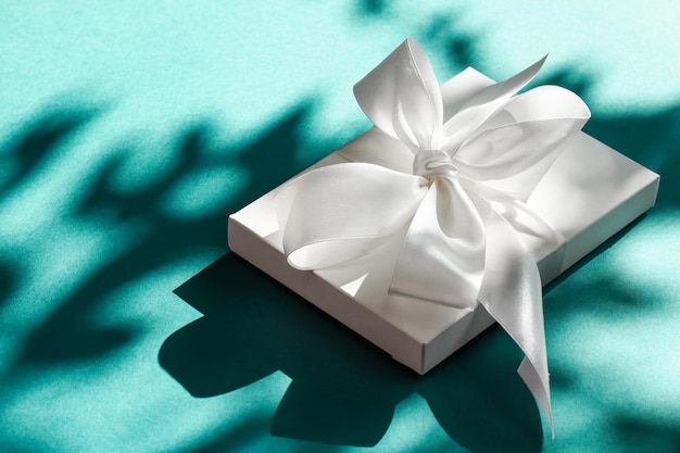 Luxury holiday white gift box with silk ribbon and bow on emerald green background luxe wedding or birthday present