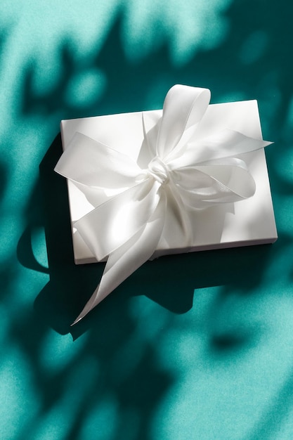 Luxury holiday white gift box with silk ribbon and bow on emerald green background luxe wedding or birthday present