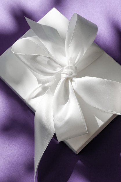 Luxury holiday white gift box with silk ribbon and bow on violet background luxe wedding or birthday present