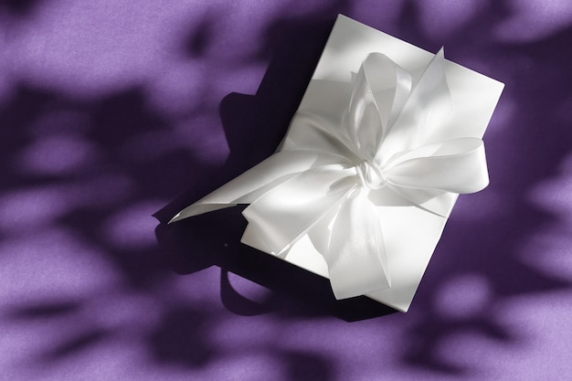 Luxury holiday white gift box with silk ribbon and bow on violet background luxe wedding or birthday present