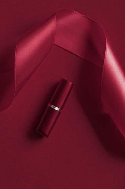 Luxury lipstick and silk ribbon on maroon holiday background makeup and cosmetics flatlay for beauty brand product design