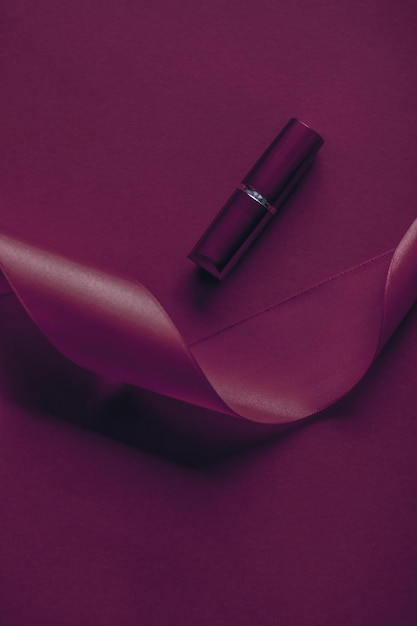 Luxury lipstick and silk ribbon on plum holiday background makeup and cosmetics flatlay for beauty brand product design