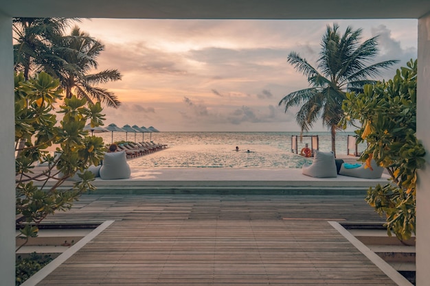 Luxury outdoor poolside, infinity swimming pool with palm trees and sunset sky beach resort