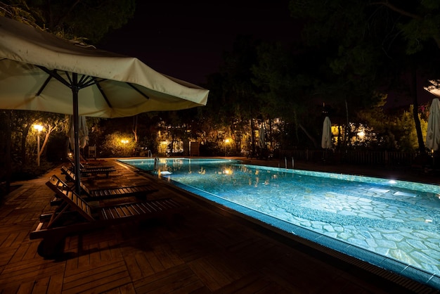 Luxury tourist resort with empty deck chairs and folded parasols by a sparkling illuminated swimming pool