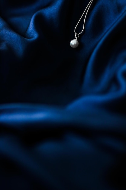 Luxury white gold pearl necklace on dark blue silk background holiday glamour jewelery present