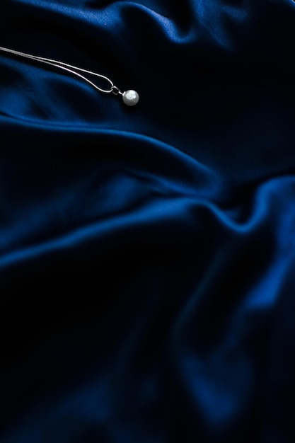 Luxury white gold pearl necklace on dark blue silk background holiday glamour jewelery present