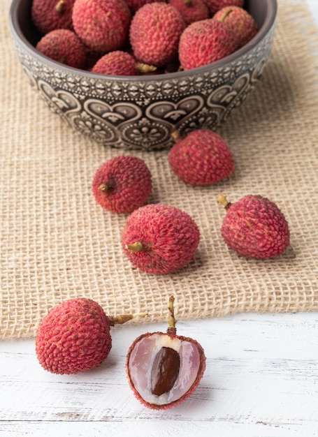 Lychees in a bowl with cut fruit over wooden table