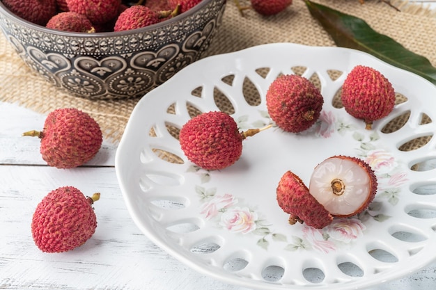 Lychees in a plate with cut fruit over wooden table