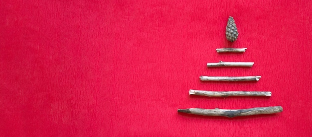 Lying on a red table is an alternative wooden Christmas tree made of simple sticks, with a cone star. Christmas and New Year background. Minimalism concept