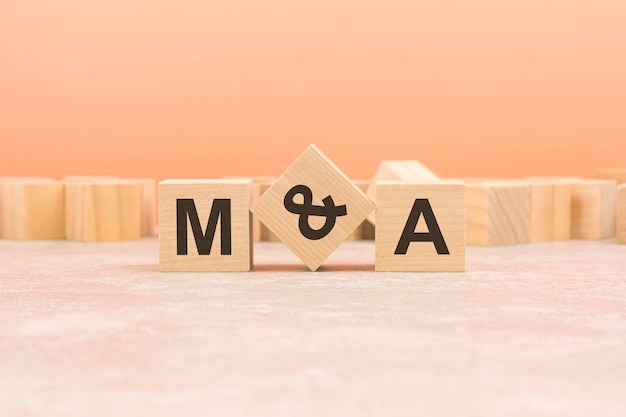 M and A wooden blocks word on orange background MA short for Mergers and Acquisitions business concept