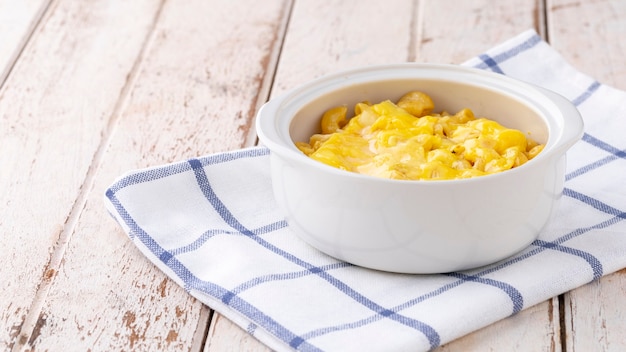 Mac and Cheese, macaroni pasta with cheese in ceramic bowl on napkin on white old wood texture background