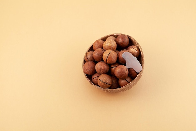 Macadamia nuts and metal key for opening nutshell in bowl on beige background