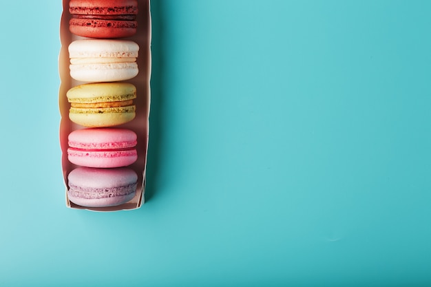 Macaroni cookies of different colors in a white box on a blue background.