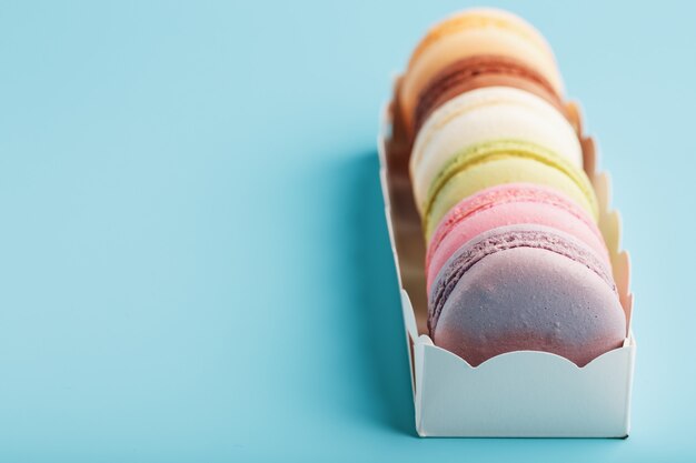 Macaroni cookies of different colors in a white box on a blue background.