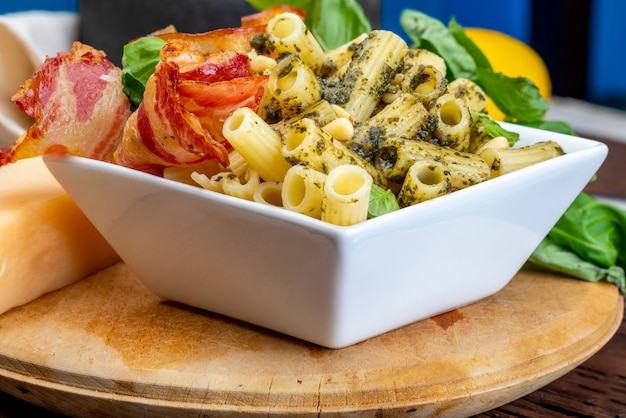 Macaroni with pesto (penne rigate). With onion and bacon, cheese, basil, pine nuts, garlic. On a wooden table with a rustic look.