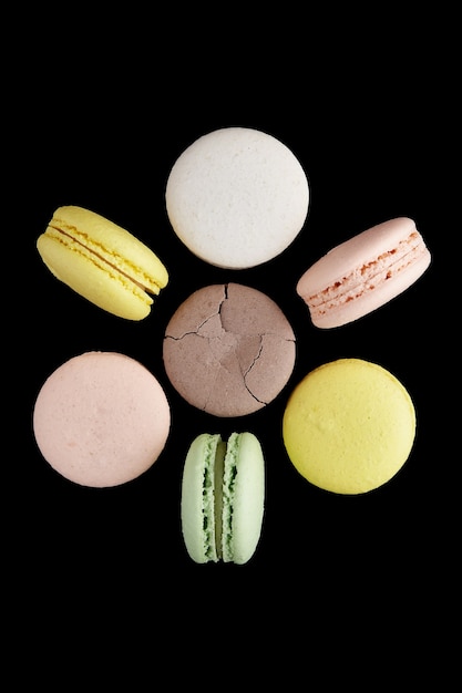 Macaroon. Six colorful cake macaron with pastel tones and one cracked lay and stand in the shape of a flower on black surface. Top view of almond cookies.