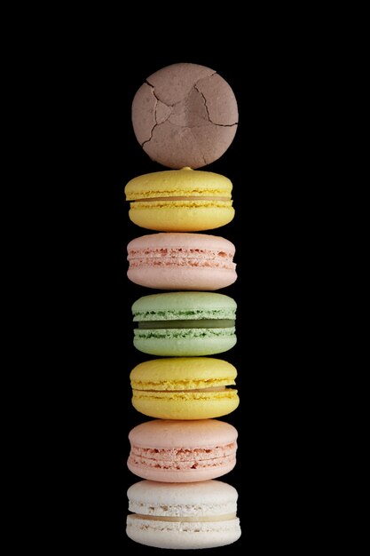 Macaroon. Stack of six colorful cake macaron with pastel tones and one cracked on black surface. Top view of almond cookies.