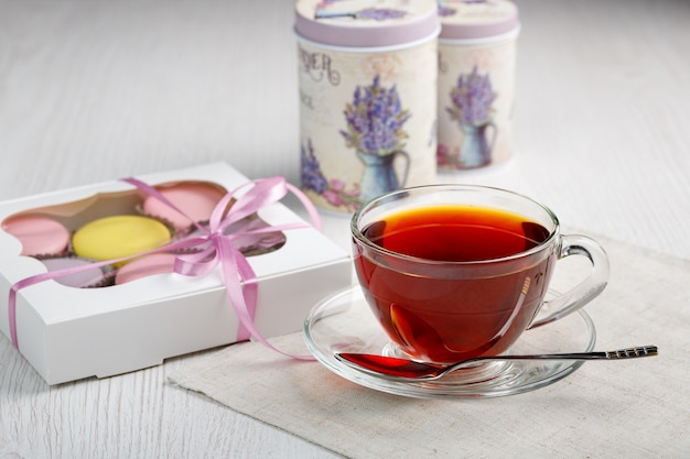 Macaroons in a box and a cup of tea on a light wood kitchen table 