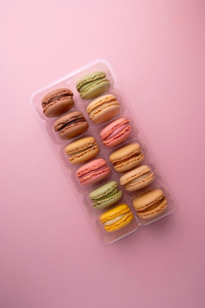 Macaroons colorful cookies in plastic box container Macarons french sweet dessert top view pink background Copy space