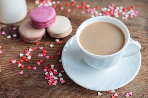 Macaroons and a cup of coffee a milk jug on a background of small hearts on a wooden background top view