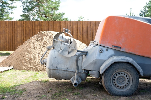 Machine with mixer isinstallation for feeding cement mixture for pouring semidry floor screed in house Construction site with slide of sand preparation for leveling the rough floor of cottage