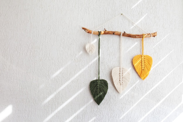 Photo macrame leaves wall hanging in yellow, white and green  and natural color on the wooden stick. cotton rope decor macrameto make your room more cozy and unique. copy space