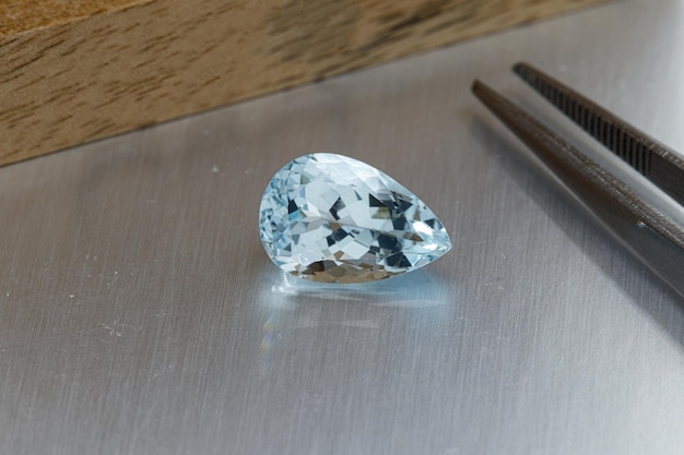 Macro mineral faceted stone aquamarine with tweezers on a gray background